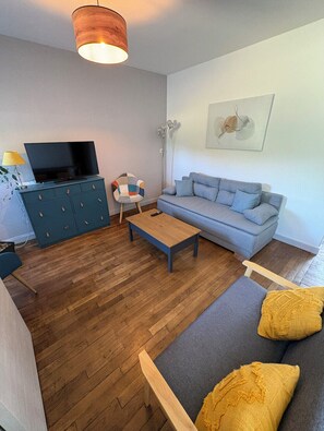 Olohuone, jossa on sohva, sohvapöytä, televisiotaso ja sen päällä televisio sekä lattiavalaisin.