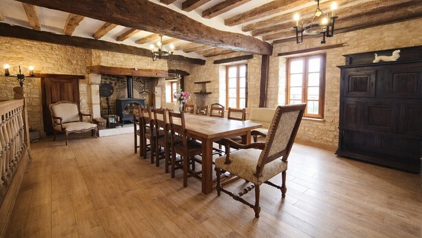 Een rustieke eethoek met een houten tafel en stoelen, stenen muren en zichtbare houten balken.