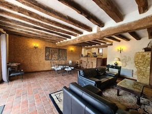 Ein rustikales Interieur mit freiliegenden Holzbalken, einem Essbereich mit Tisch und Stühlen, einem Ledersofa und einem gemusterten Teppich.