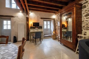 Ein gemütlicher Raum mit Holzbalkendecke, Steinwänden, einem großen Spiegel, einem Schreibtisch mit Fernseher und einer komfortablen Sitzecke.