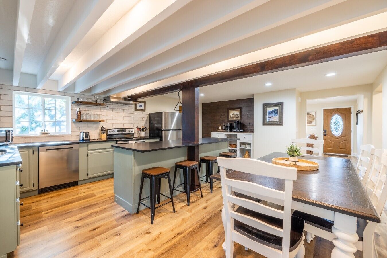 A modern kitchen with a central island, bar stools, and a dining area with a wooden table and white chairs.