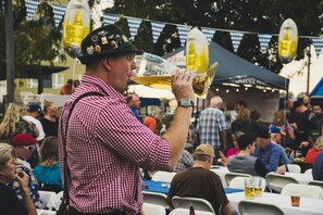 Eine Person mit kariertem Hemd und einer Mütze mit Abzeichen, die einen großen Bierkrug hält.