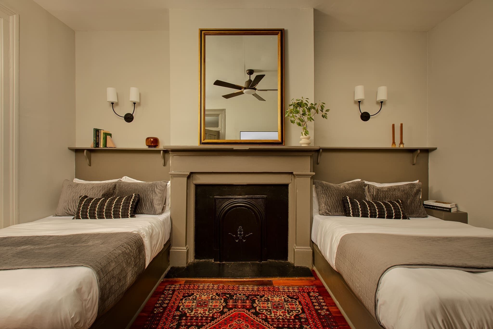 A hotel room with two beds, a fireplace, a ceiling fan, and wall-mounted sconces.