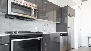 Een moderne keuken met roestvrijstalen apparatuur, grijze keukenkastjes en een betegelde achterwand.