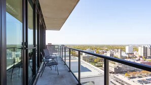 Een balkon met glazen hekwerk, met uitzicht op een stadsgezicht met gebouwen en bomen.