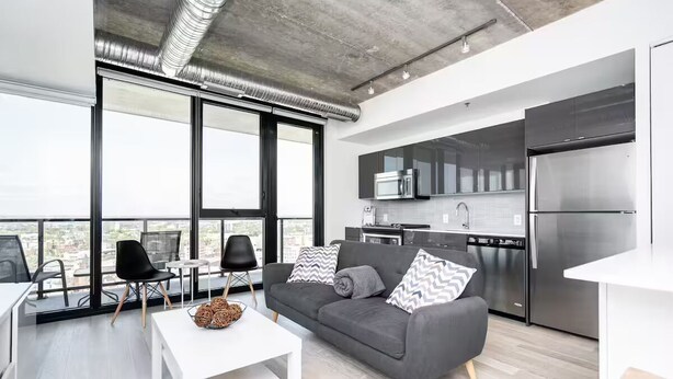 Een modern appartement met balkon, een keuken met roestvrijstalen apparatuur, en een grijze bank met decoratieve kussens.