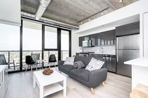 Un appartement moderne doté d’un balcon, d’une cuisine équipée d’appareils électroménagers en acier inoxydable et d’un canapé gris agrémenté de coussins à motifs.