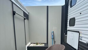 A small outdoor patio area with two wicker chairs, a small planter with flowers, and a camper trailer.