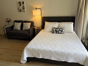 Une chambre à coucher avec un grand lit, un canapé, une lampe et une petite table sur laquelle est posé un vase de fleurs.