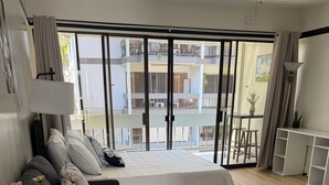 Ein modernes Schlafzimmer mit einem großen Bett, einer Couch, einem kleinen Tisch mit Blumenvase und Blick auf den Balkon.