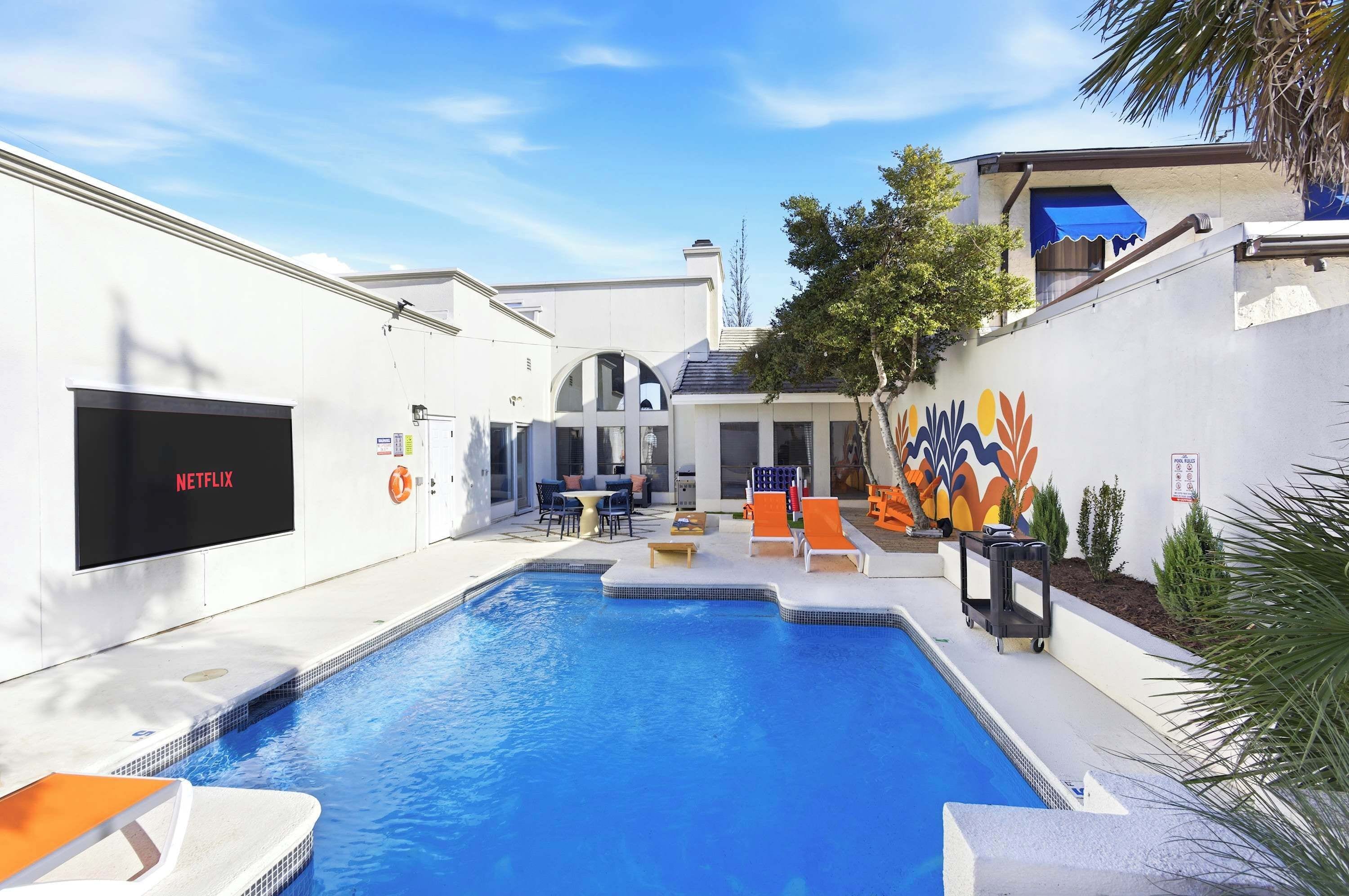 A swimming pool with lounge chairs and a TV screen displaying 'NETFLIX'.