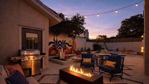 Patio esterno con barbecue, braciere, posti a sedere e luci decorative.