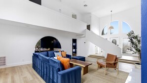 Un ampio soggiorno con un divano blu, un tavolino in legno e una poltrona in pelle marrone. Una scala conduce a un livello superiore.
