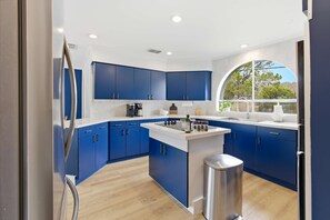 A modern kitchen with blue cabinets, a central island, and a stainless steel trash can. - Outdoor Oasis • Poolside Movie Nights • Sleeps 14 (San Antonio)