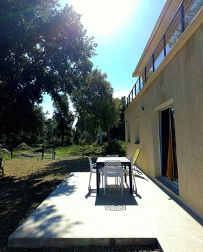 Un espace extérieur aménagé en patio, avec une table et des chaises, un sol en béton et un bâtiment doté d’une fenêtre et d’une porte.
