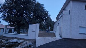 Un edificio residencial con entrada para vehículos, buzón y un gran árbol de fondo.