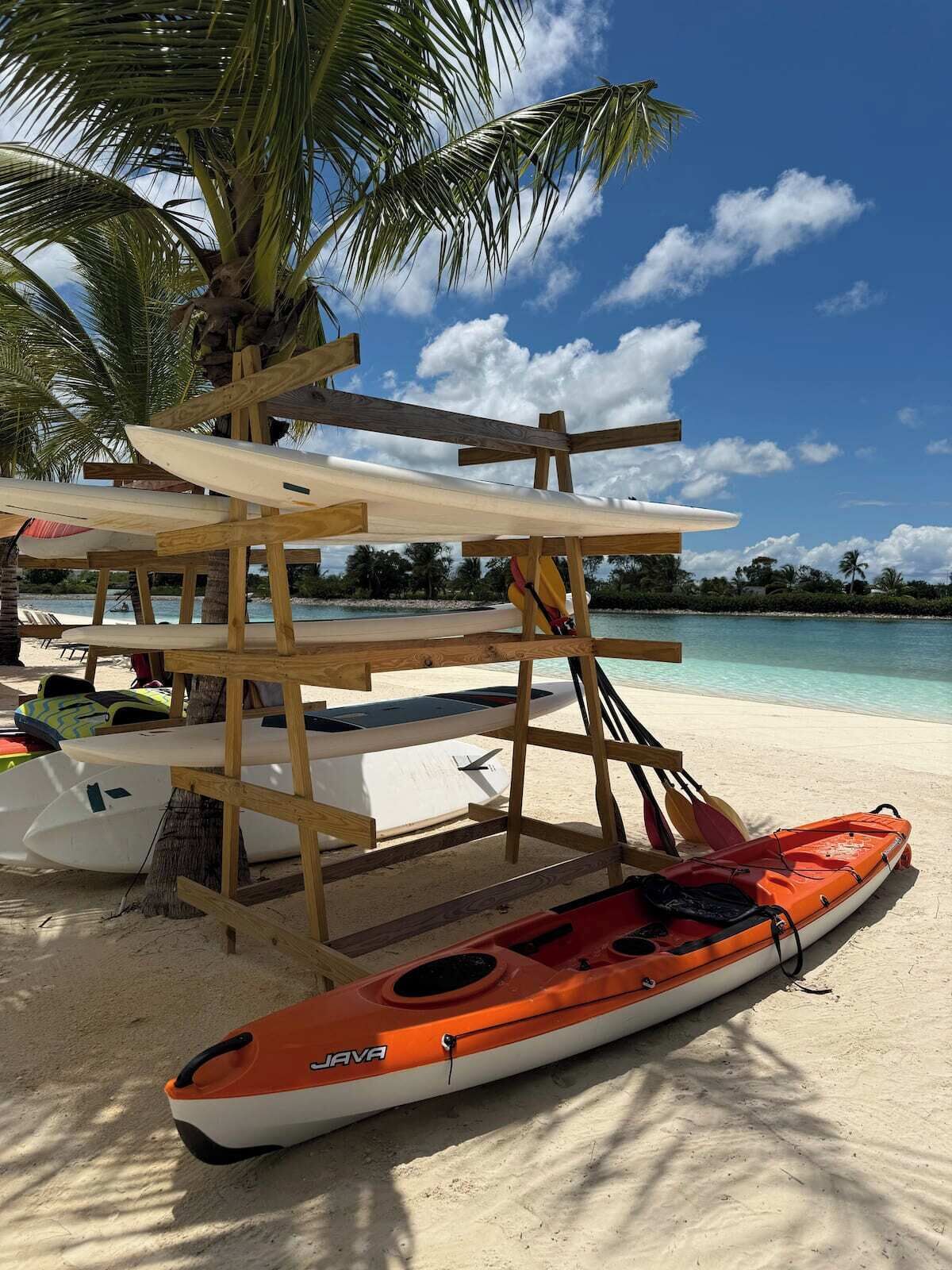 A beach with a wooden structure holding surfboards and a kayak.