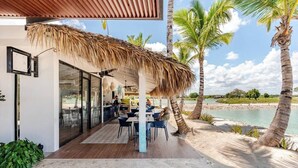 A modern outdoor dining area with a thatched roof, palm trees, and a view of the beach. - Prestige Golf Villa Privad Pool Privad Pool vista cana- Punta cana (Punta Cana)