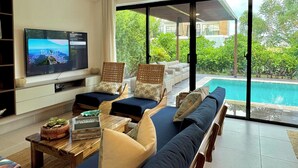 A modern living room with a television, comfortable seating, a coffee table, and a view of a swimming pool. - Prestige Golf Villa Privad Pool Privad Pool vista cana- Punta cana (Punta Cana)