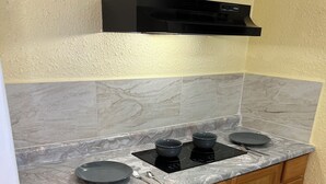 A compact kitchen with a marble countertop, wooden cabinets, and a black range hood.