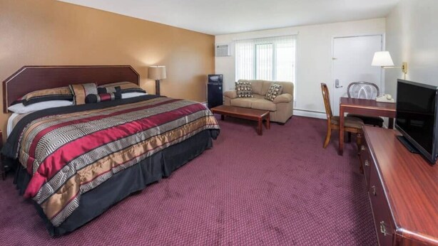 A hotel room with a large bed, a sofa, a TV, and a desk.