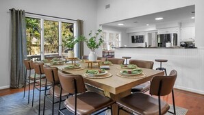 A dining area with a large table set for six, surrounded by chairs, with a view of the outdoors through large windows. - The Breakaway on Lake Hamilton | Hot Tub, Kayaks! (Hot Springs National Park)