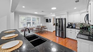 A modern kitchen with a black countertop, stainless steel appliances, and a dining area with bar stools. - The Breakaway on Lake Hamilton | Hot Tub, Kayaks! (Hot Springs National Park)