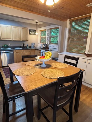Una mesa de comedor con manteles individuales, un frutero y una cocina al fondo.