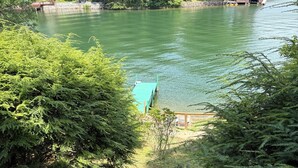 Ein ruhiger See, umgeben von dichtem Grün, eine Anlegestelle und ein kleines Gebäude.