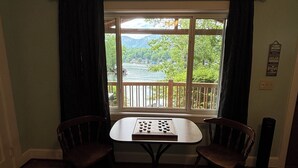 Ein Zimmer mit einem Tisch, zwei Stühlen, einem Fenster mit Vorhängen, einem Teppich und einer Wandleuchte.
