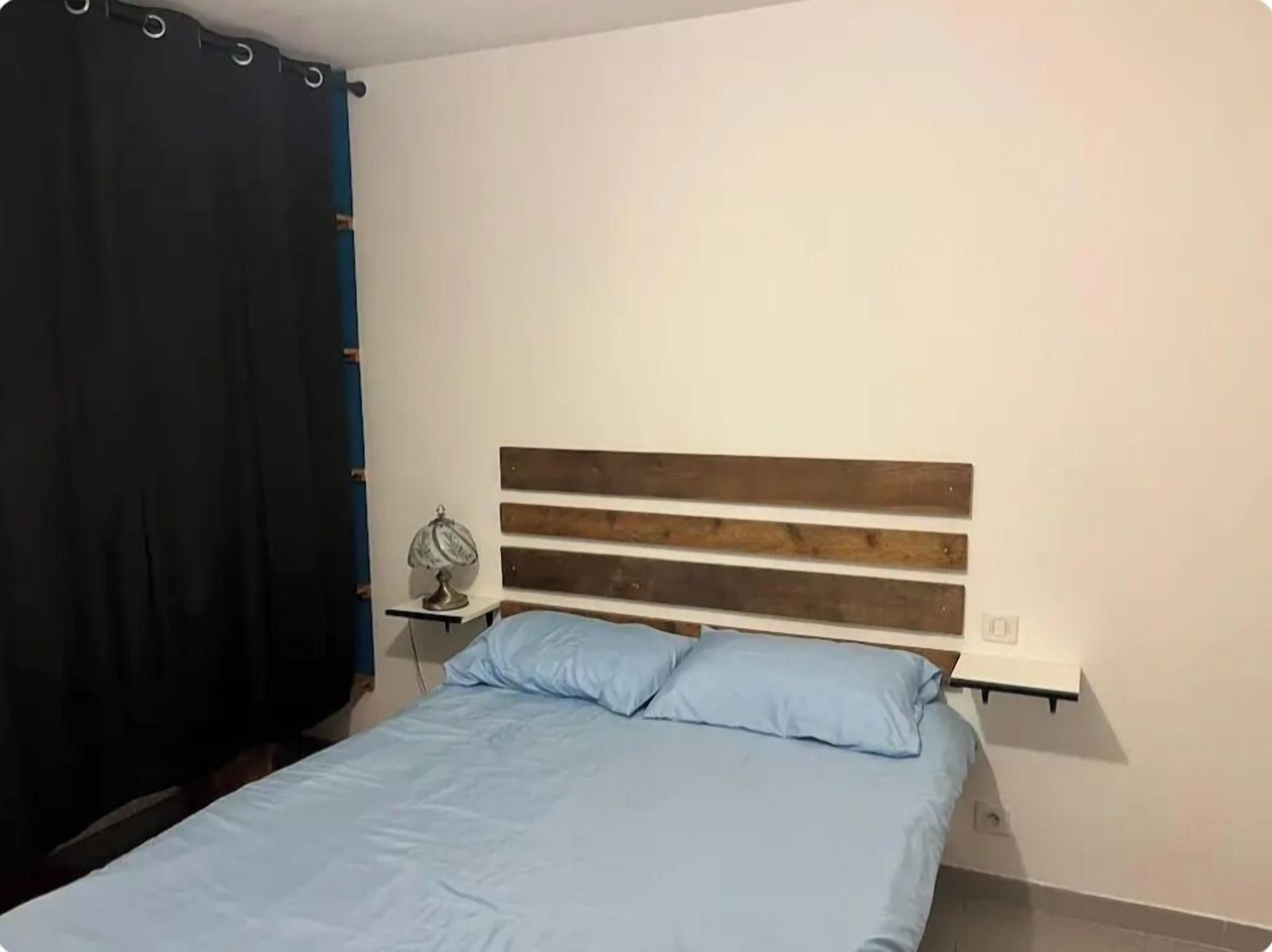 A bedroom with a bed, a nightstand, a lamp, and a curtain.