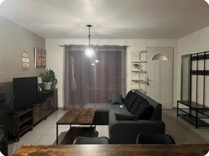 A living room with a sofa, a coffee table, a TV, a cabinet, and a door with a shelf above it.