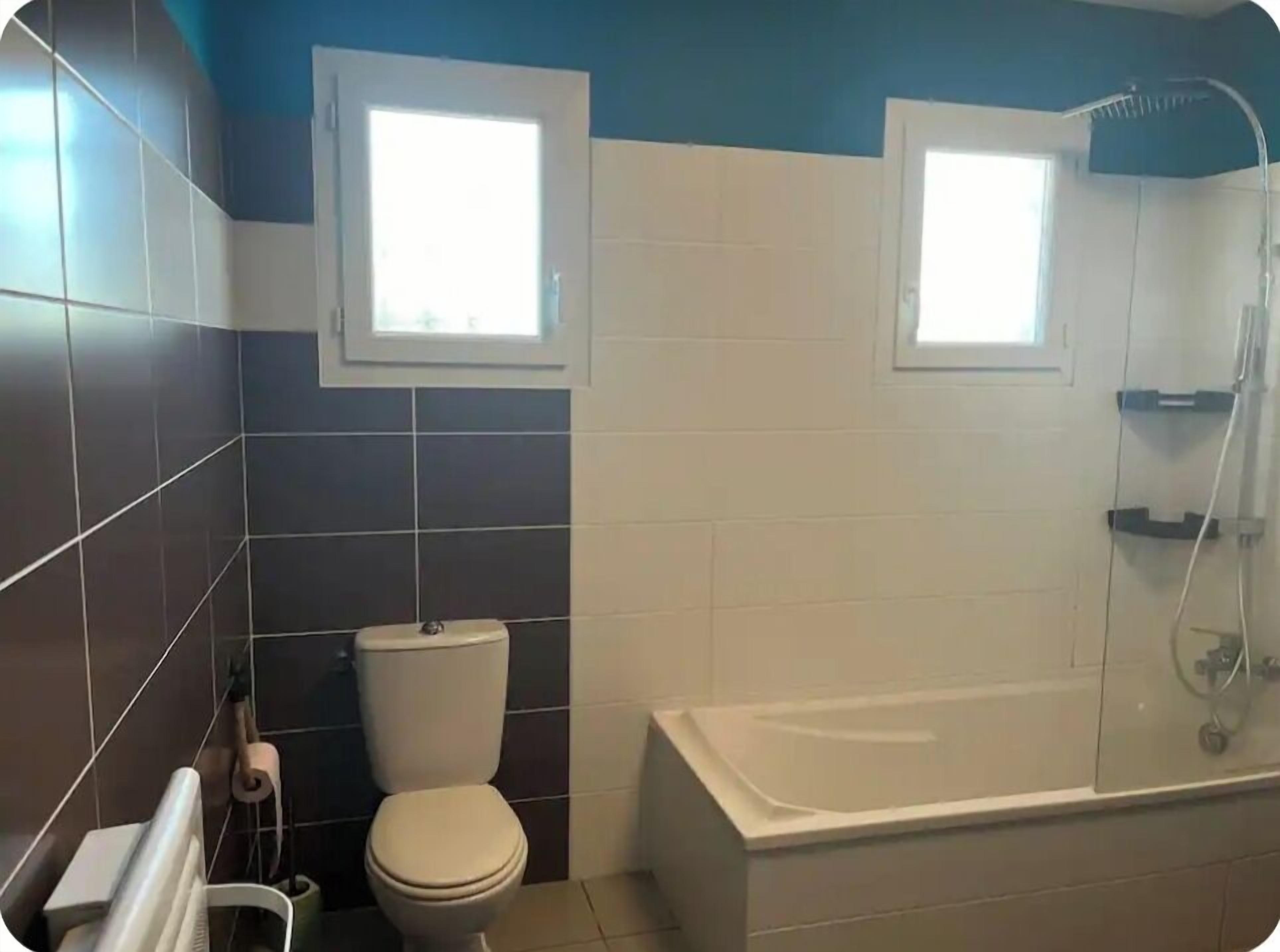A bathroom with two windows, a toilet, and a bathtub.