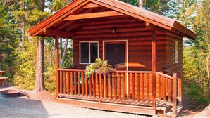 A wooden cabin with a porch, surrounded by trees.