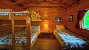 A cabin with two bunk beds, a single bed, wooden walls, a ceiling light, and a window with curtains.