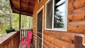 Una cabaña de madera con un porche, una silla Adirondack roja y una ventana.