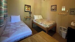 Una habitación con dos camas, una mesa de madera, un pequeño estante con una lámpara y un cuadro en la pared.