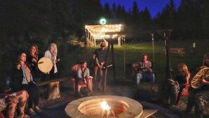 A group of people around a campfire at night, with a covered structure in the background. - Cute Camper on FHU Site in Beautiful Campground (Hungry Horse)