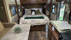 A compact RV interior with a bed, a small kitchenette, and a seating area. - Cute Camper on FHU Site in Beautiful Campground (Hungry Horse)