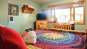 A cozy room with a colorful circular rug, a television, a wooden chair, and a window with a view of the outdoors. - Lodge Room with Views of Glacier NP (Hungry Horse)