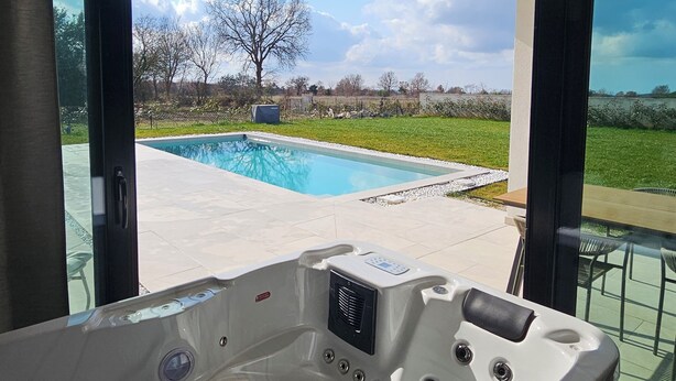 A modern bathroom with a large bathtub, a glass shower enclosure, and a view of a swimming pool and garden. - One of a kind villa 2+1 guests with heated pool and indoor wellness area (Svetvincenat)