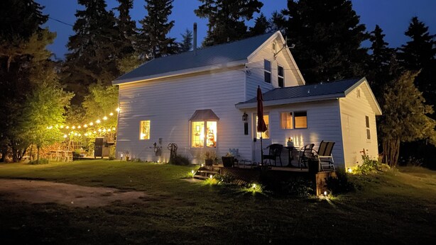 Ein weißes, zweistöckiges Haus mit Veranda, Sitzgelegenheiten im Freien und Lichterketten.