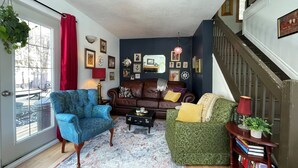 Ein Wohnzimmer mit einem braunen Ledersofa, einem blauen Sessel, einem grünen Sessel, einem gemusterten Teppich und einer Treppe.