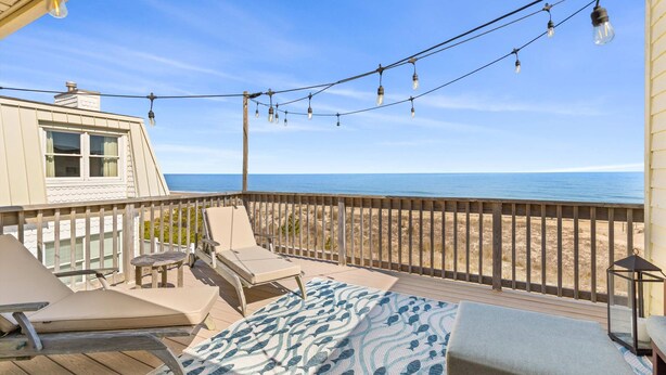 Eine Terrasse mit Liegestühlen und einem gemusterten Teppich mit Blick auf einen Strand.