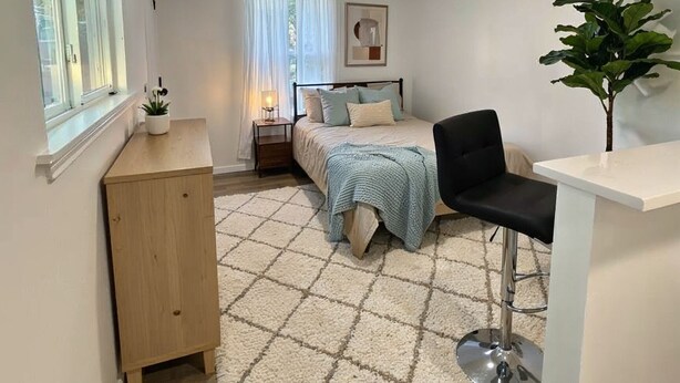 Una habitación pequeña y acogedora con cama, mesita de noche, silla y un espacio de escritorio.