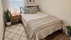 Un dormitorio con cama, mesita de noche, lámpara y un cuadro en la pared.