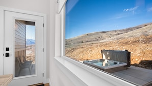 Een kamer met een groot raam met uitzicht op een rotsachtig landschap, een schuifdeur en een hottub buiten.