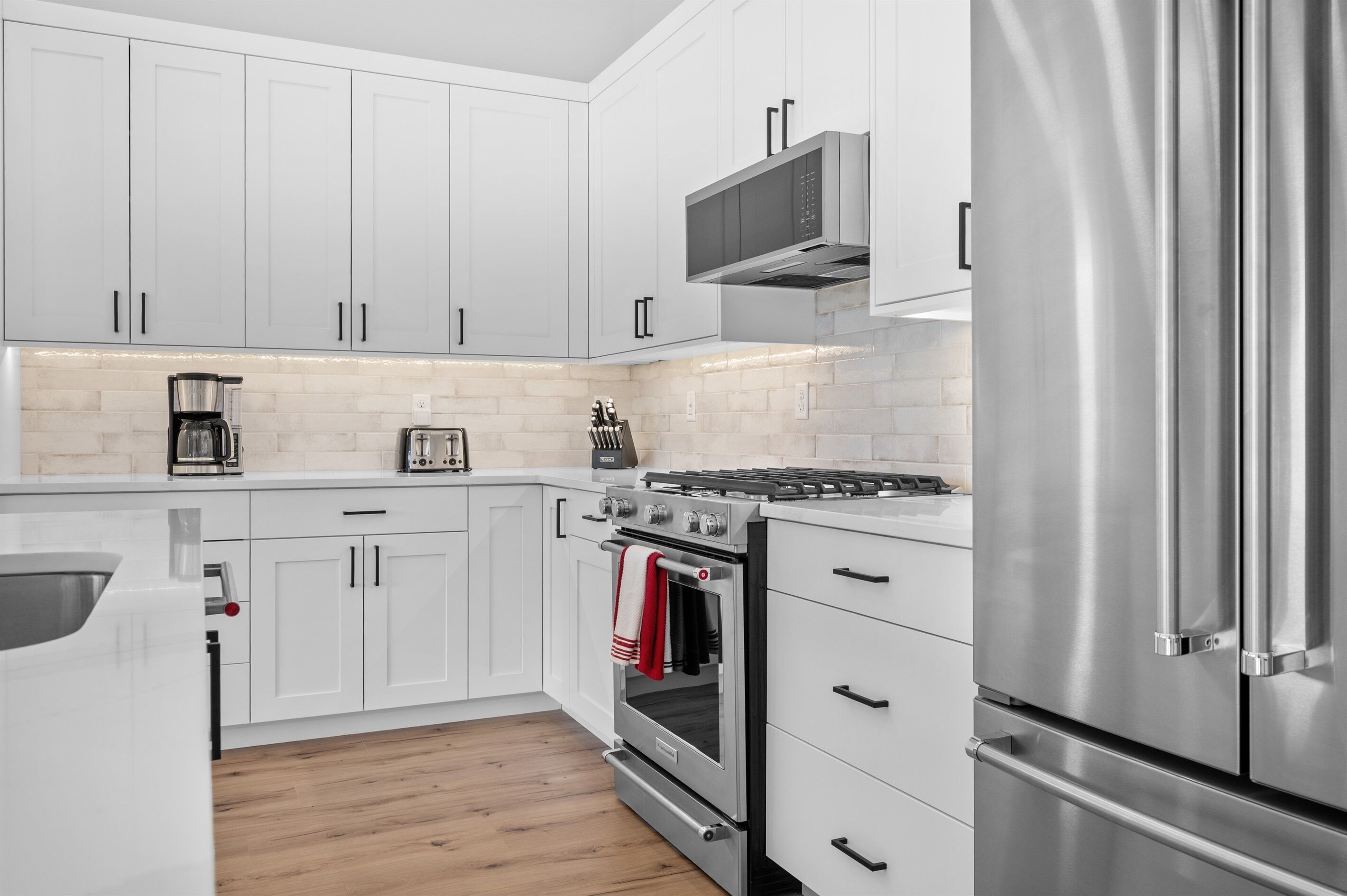 A modern kitchen with white cabinets, a stainless steel refrigerator, a built-in oven, and a microwave.