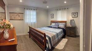 A bedroom with a wooden bed, a bedside table, a nightstand, a lamp, and a vase with flowers.
