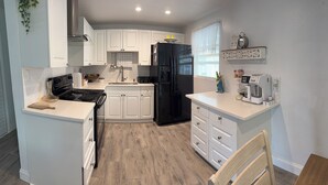 A modern kitchen with white cabinetry, a black refrigerator, a coffee maker, and a wooden chair.